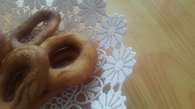 Closeup view of a set of freshly prepared donuts served on white changair. Donuts are placed in a changair over wooden floor