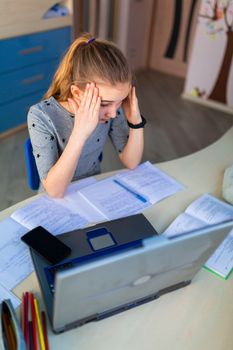 Beautiful young school girl working at home in her room with a laptop and class notes studying in a virtual class. Distance education and learning, e-learning, online learning concept during quarantine