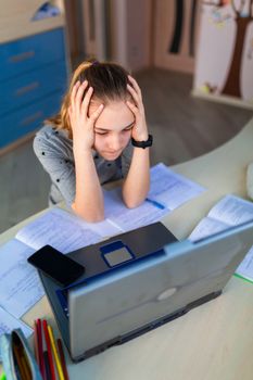 Beautiful young school girl working at home in her room with a laptop and class notes studying in a virtual class. Distance education and learning, e-learning, online learning concept during quarantine