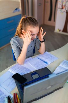 Beautiful young school girl working at home in her room with a laptop and class notes studying in a virtual class. Distance education and learning, e-learning, online learning concept during quarantine