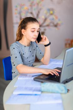 Beautiful young school girl working at home in her room with a laptop and class notes studying in a virtual class. Distance education and learning, e-learning, online learning concept during quarantine