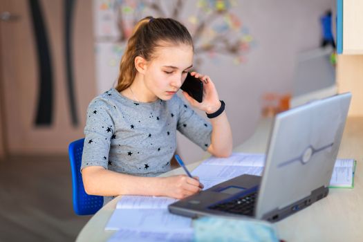 Beautiful young school girl working at home in her room with a laptop and class notes studying in a virtual class. Distance education and learning, e-learning, online learning concept during quarantine