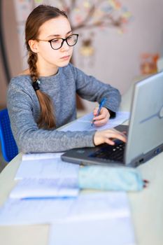 Beautiful young school girl left-handed working at home in her room with a laptop and class notes studying in a virtual class. Distance education and learning, e-learning, online learning concept during quarantine