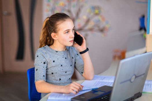 Beautiful young school girl working at home in her room with a laptop and class notes studying in a virtual class. Distance education and learning, e-learning, online learning concept during quarantine