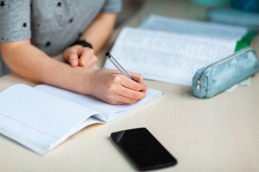 Close up of young school girl working at home in her room with class notes checking mobile phone and studying. Distance education and learning concept during quarantine