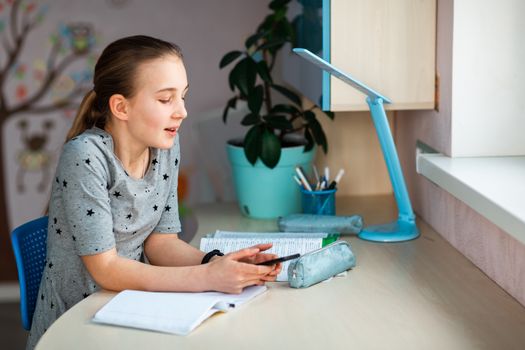 Beautiful young school girl working at home in her room with class notes checking mobile phone and studying. Distance education and learning concept during quarantine