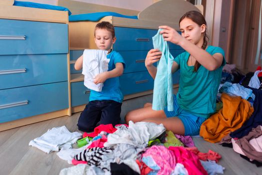 Happy children folding clothes in thier messy bedroom