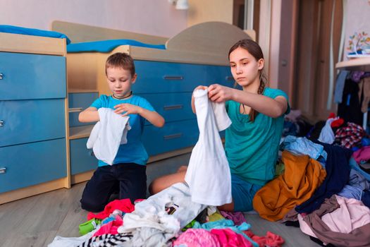 Happy children folding clothes in thier messy bedroom