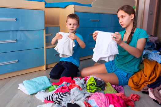 Happy children folding clothes in thier messy bedroom