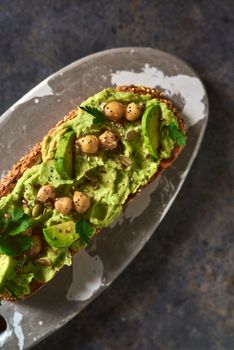 Toast of avocado hummus, decorated with chickpeas on stone table