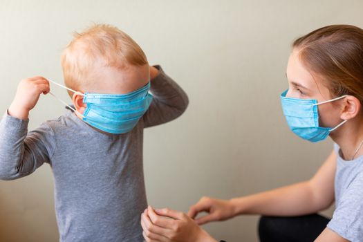 Teenage girl helping to his baby brother to wear a medical mask. Coronavirus protection, wearing masks concept