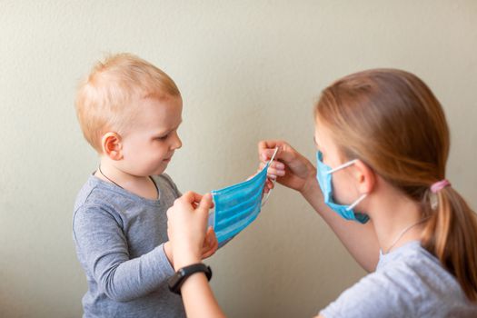 Teenage girl helping to his baby brother to wear a medical mask. Coronavirus protection, wearing masks concept