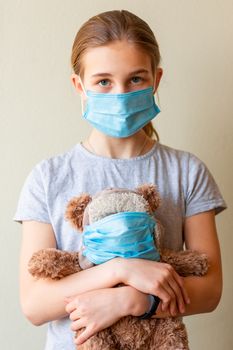 Little teenage girl with teddy bear toy both in medical masks sad and scared. Coronavirus protection, wearing masks concept