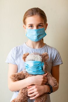 Little teenage girl with teddy bear toy both in medical masks sad and scared. Coronavirus protection, wearing masks concept