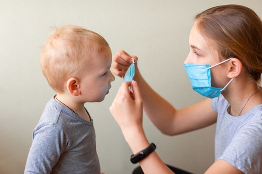 Teenage girl helping to his baby brother to wear a medical mask. Coronavirus protection, wearing masks concept