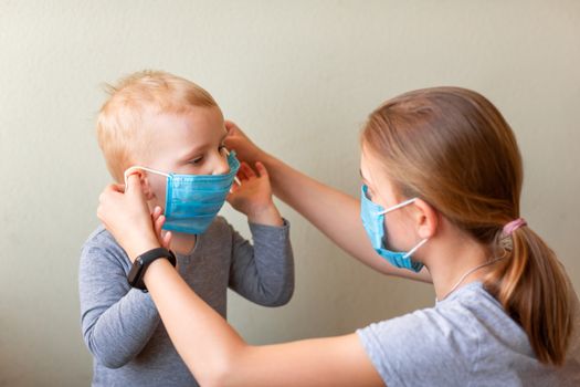 Teenage girl helping to his baby brother to wear a medical mask. Coronavirus protection, wearing masks concept