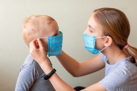 Teenage girl helping to his baby brother to wear a medical mask. Coronavirus protection, wearing masks concept