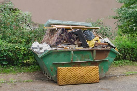 Green container with household waste against the green wood