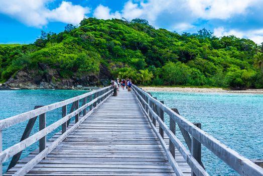 Yasawa-I-Rara, Fiji--March 8, 2018. Tourists on their way to a Fiji beach are walking down a long wooden dock toward lush island foliage.