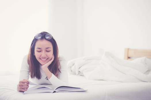 charming woman lying on bed reading a book in bedroom.