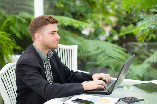 businessman and smiling, as he work on his laptop in the living room.