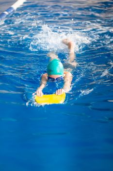 Cute little girl swimmer training in a swimming pool in glasses with a swimming kickboard. Swimming sport for kids concept