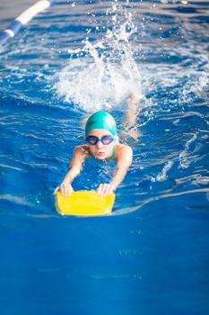 Cute little girl swimmer training in a swimming pool in glasses with a swimming kickboard. Swimming sport for kids concept