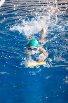 Cute little girl swimmer training in a swimming pool in glasses with a swimming kickboard. Swimming sport for kids concept