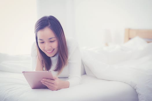 woman lying in bedroom with digital tablet touching with finger in morning sunlight
