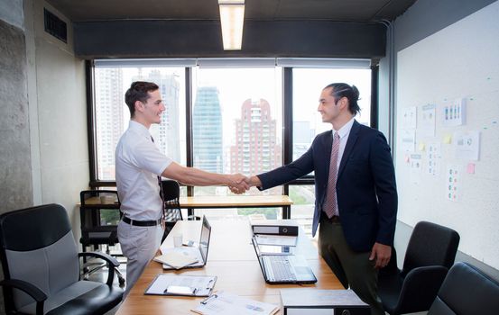 Two happy successful business partner shaking hands in the office.