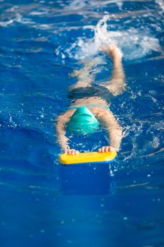 Cute little girl swimmer training in a swimming pool in glasses with a swimming kickboard. Swimming sport for kids concept