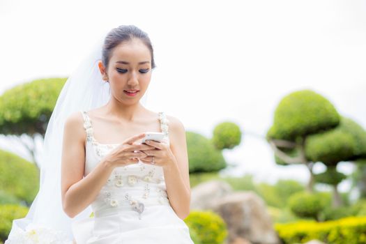 bride touch on phone in wedding dress on garden.