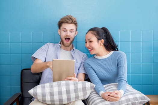 Cute loving couple is using tablet in sofa - They are sitting and smiling and glad with success.