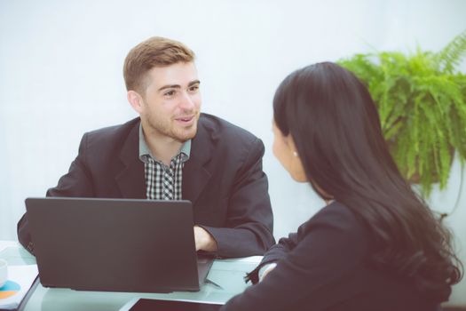 Couple of young business working at modern office, two coworkers discussing fun project over a laptop.