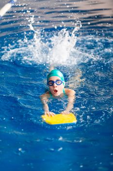 Cute little girl swimmer training in a swimming pool in glasses with a swimming kickboard. Swimming sport for kids concept