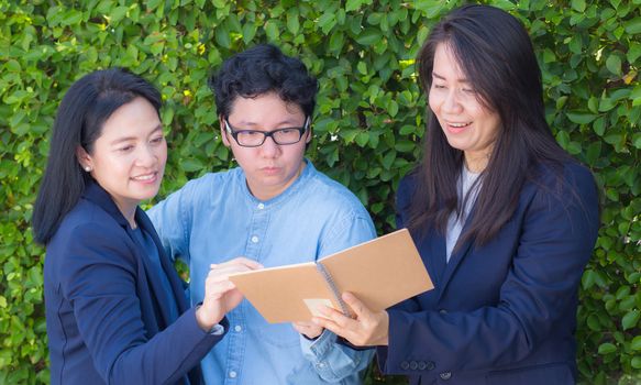 Businesswomen three people looking information on notebook or diary corporate on tree wall.