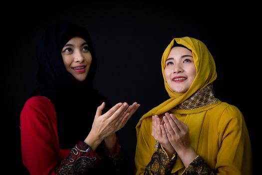 religious young Muslim two women praying over black background.