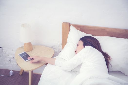Hand of sleepy woman waking up with alarm clock on mobile phone in bedroom.