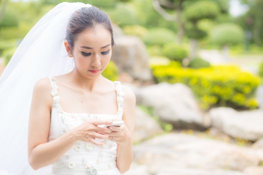 bride touch on phone in wedding dress on garden.