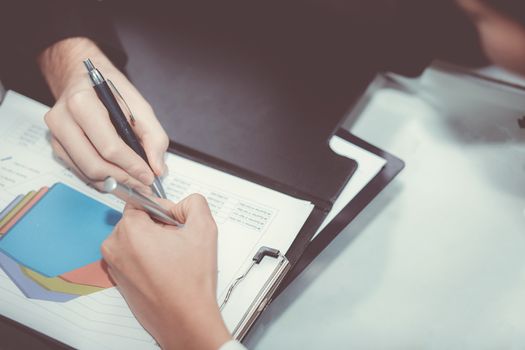 Closeup of business partners hands over document with charts and graph of male and woman hand with pens in meeting room.