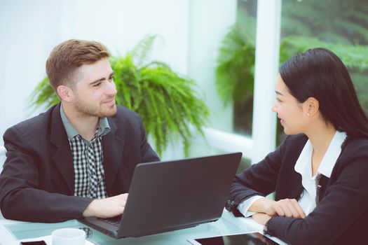 Couple of young business working at modern office, two coworkers discussing fun project over a laptop.