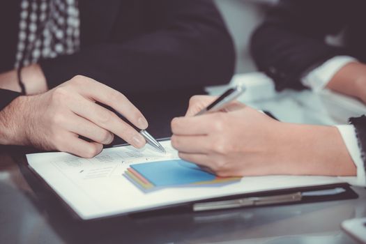 Closeup of business partners hands over document with charts and graph of male and woman hand with pens in meeting room.