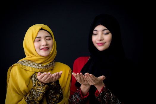 religious young Muslim two women praying over black background.