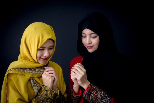 religious young Muslim two women praying over black background.