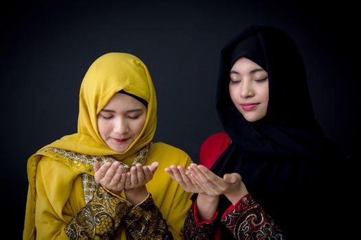 religious young Muslim two women praying over black background.