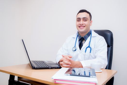 confident male doctor sitting at office desk and smiling, medical healthcare concept.