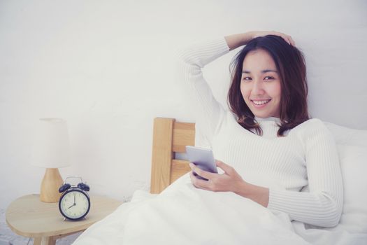woman asian model holding a mobile phone with wake up in bedroom.