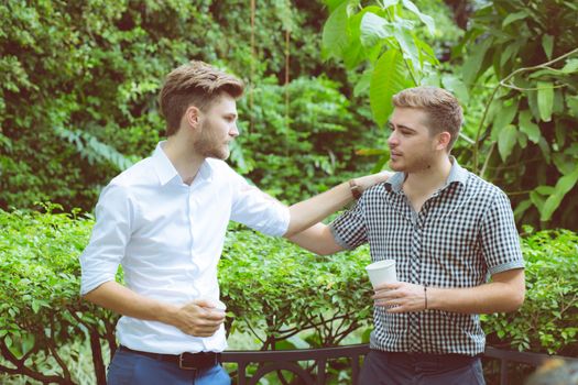 Two friends men talking standing in a garden.