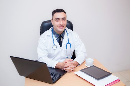 confident male doctor sitting at office desk and smiling, medical healthcare concept.