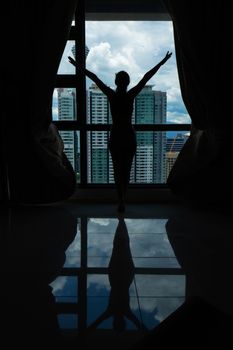 A slender girl is looking at the city through a large window. High floor